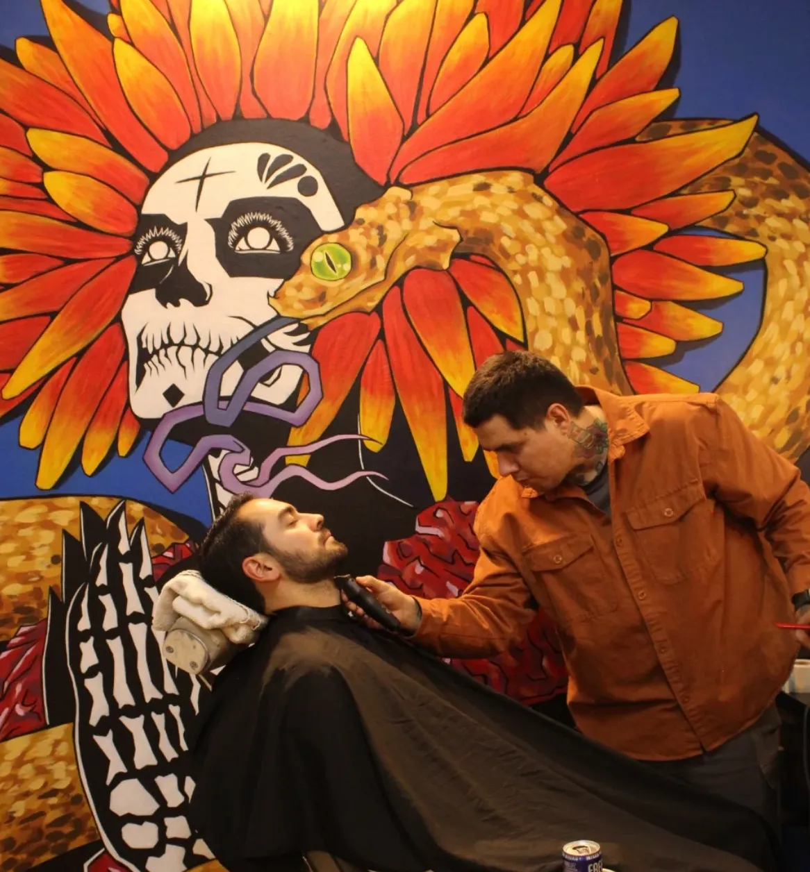 Barbero terminando un corte frente al mural de la catrina